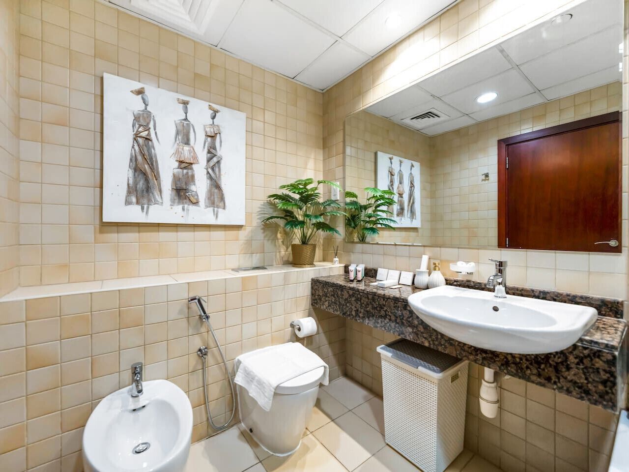 Un bagno con bidet, servizi igienici, lavandino e due piante in vaso.