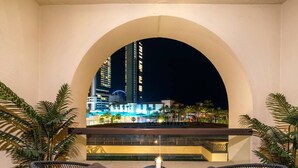 Uma varanda com duas cadeiras de vime e uma mesa pequena, com vista para um horizonte urbano à noite.