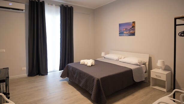 A modern hotel room with a large bed, a bedside table with a lamp, a chair, and a painting on the wall. - Bivio 281 suite&rooms (Carini)