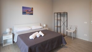 A neatly arranged hotel room with a large bed, a nightstand, a chair, and a wardrobe. - Bivio 281 suite&rooms (Carini)