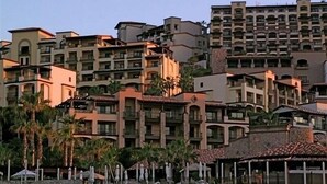 Un hotel de varios pisos con balcones, fachada de piedra y palmeras.