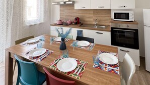 A modern kitchen with white cabinets, a microwave, oven, and a dining area with a wooden table set for four. - Grandma pina mondello house (Palermo)