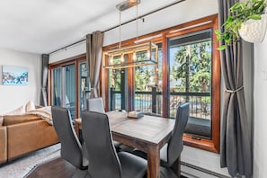 A modern living room with a dining table, chairs, a sofa, and large windows with curtains. - Walk to Main St | Pool & Hot Tub (Breckenridge)