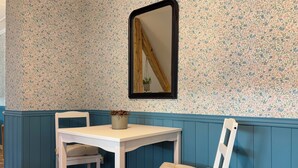 A room with a white table and two chairs, a mirror on the wall, and floral patterned wallpaper. - English cottage - Atypical accommodation (Sarreguemines)