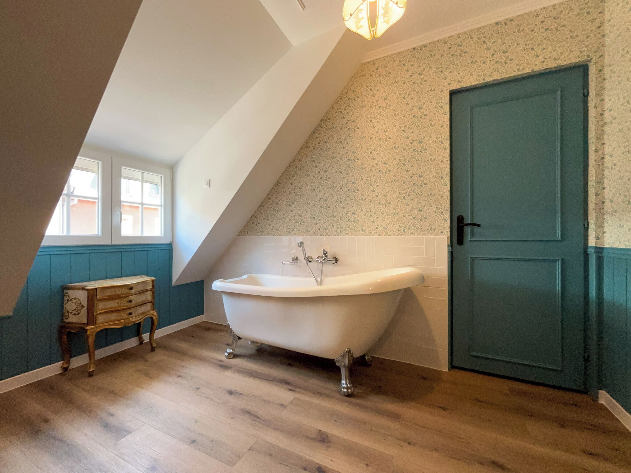 A bathroom with a freestanding bathtub, a wooden chest of drawers, a door, and a window.