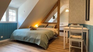 A bedroom with a sloped ceiling, a bed with a green bedspread, a white chair, and a small table. - English cottage - Atypical accommodation (Sarreguemines)