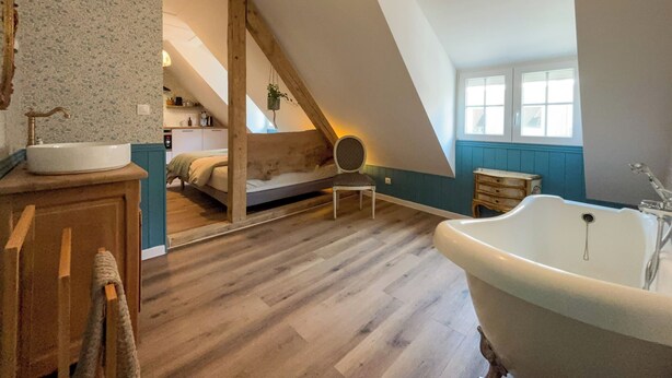 A loft bedroom with a sloped ceiling, a wooden bed, a white bathtub, and a small window. - English cottage - Atypical accommodation (Sarreguemines)