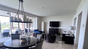Un salón espacioso con una mesa redonda de comedor, asientos cómodos, un televisor de pantalla plana y un ventanal con vistas al exterior.