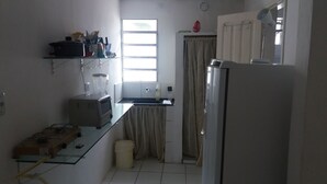 A compact kitchen with a refrigerator, microwave, and a small sink. There is a window providing natural light, and a curtain covers the door.