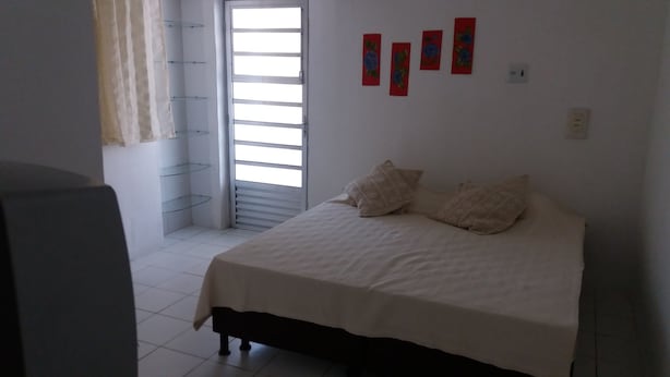 A bedroom with a bed, pillows, a window, and a wall with artwork.