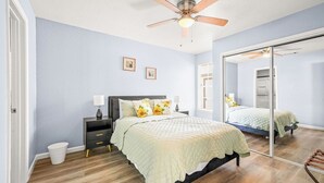 A bedroom with a bed, bedside tables, a ceiling fan, and a large mirror.
