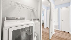 A laundry room with a Samsung washer and dryer, a drying rack, and a door leading to another room.