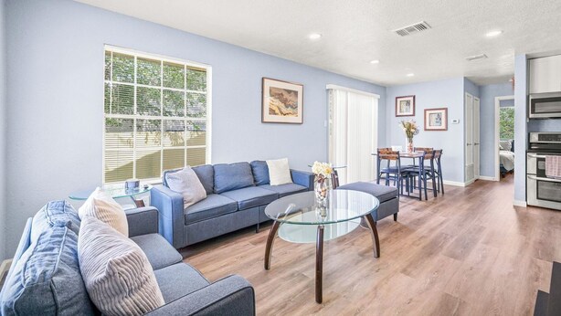 A modern living room with a blue sofa, a glass coffee table, and a dining area with a table and chairs.