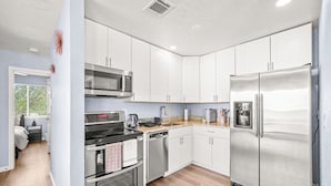 A modern kitchen with white cabinets, stainless steel appliances, and a wooden countertop.