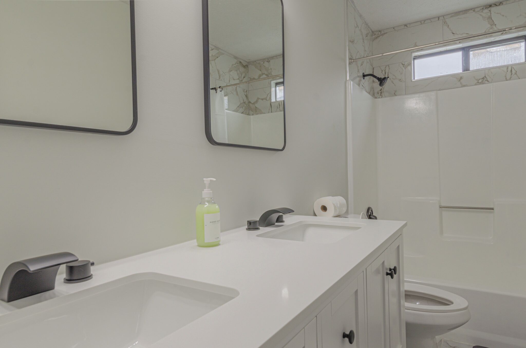 A modern bathroom with two sinks, a mirror, a toilet, and a shower area.