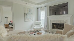 Un salon avec une cheminée blanche, un grand téléviseur fixé au-dessus, et un canapé blanc moelleux.