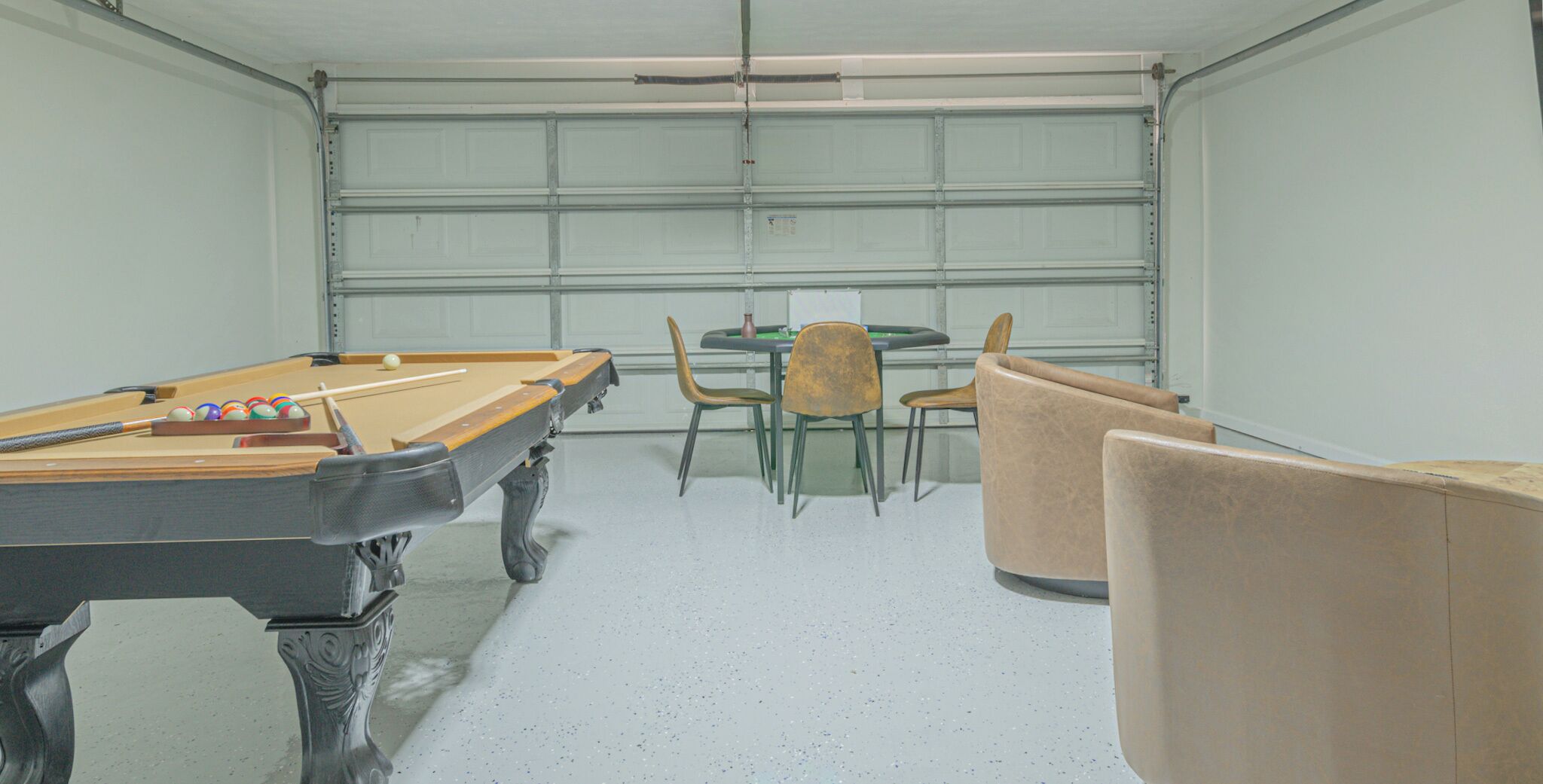 A pool table with chairs and a table in a room with a garage door.