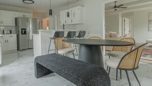 Une cuisine moderne avec des meubles blancs, un réfrigérateur en acier inoxydable, une table de salle à manger ronde avec quatre chaises et un banc.