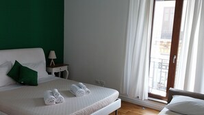 Habitación de hotel con cama, mesita de noche, lámpara, ventana con cortinas y vistas al exterior.