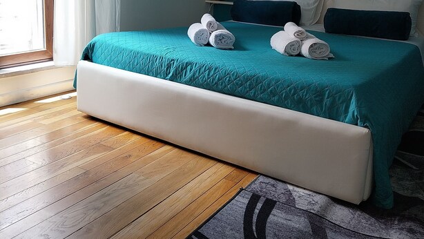 Un dormitorio con colcha color turquesa, cabecera blanca y suelo de madera.