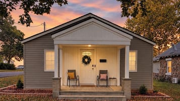 A single-story house with a front porch, a wreath above the door, and two chairs.