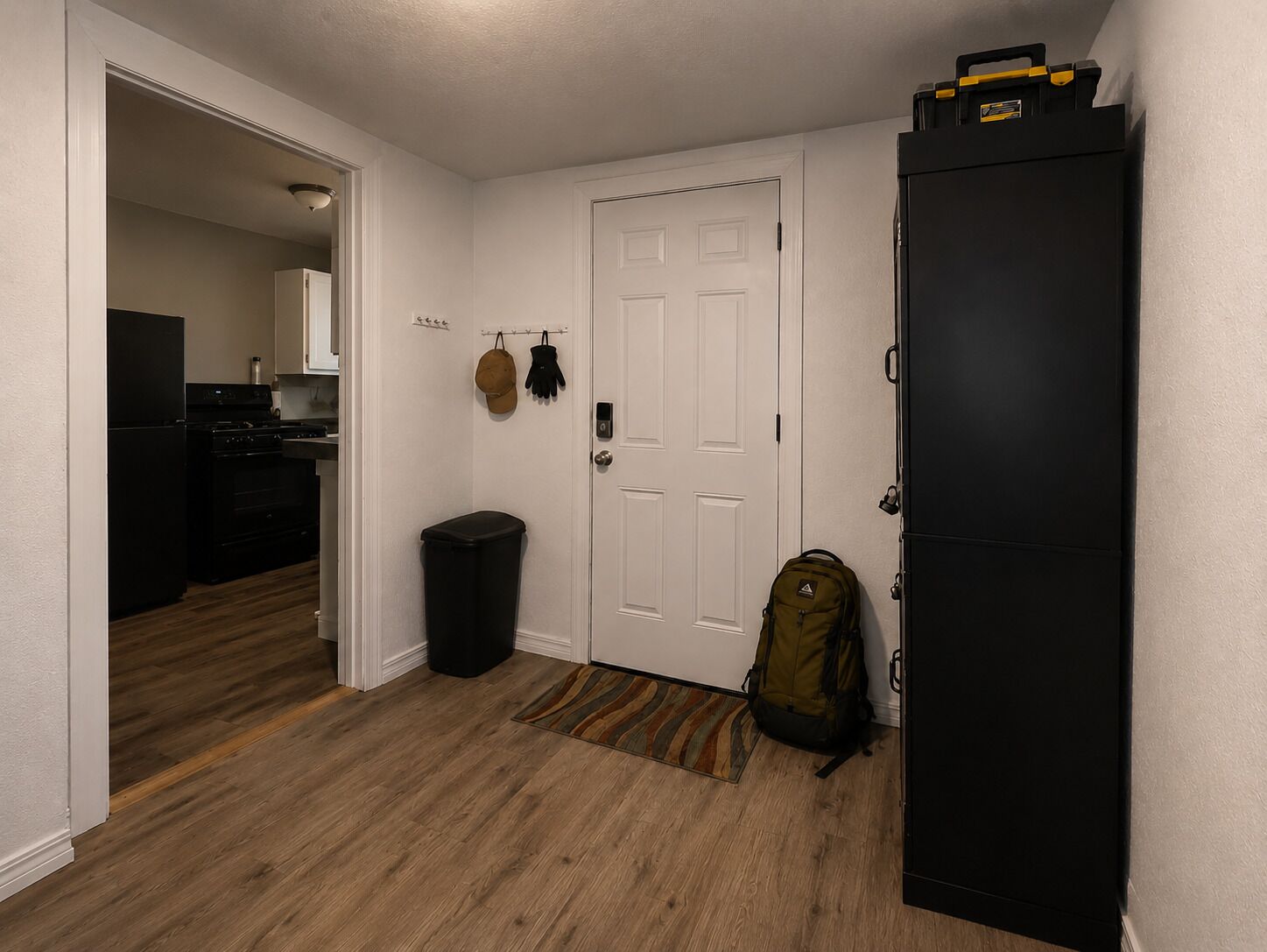 A hallway with a black refrigerator, a trash bin, and a backpack on the floor.