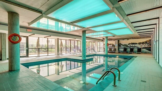 An indoor swimming pool with clear glass walls, a lifeguard chair, and a view of the outside. - Montreal - C Lofts Le Smith 2 Bedroom (Montréal)