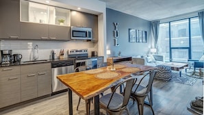A modern kitchen with built-in appliances, a dining area with a wooden table, and a living room with a sofa and large windows. - Montreal - C Lofts Le Smith 2 Bedroom (Montréal)