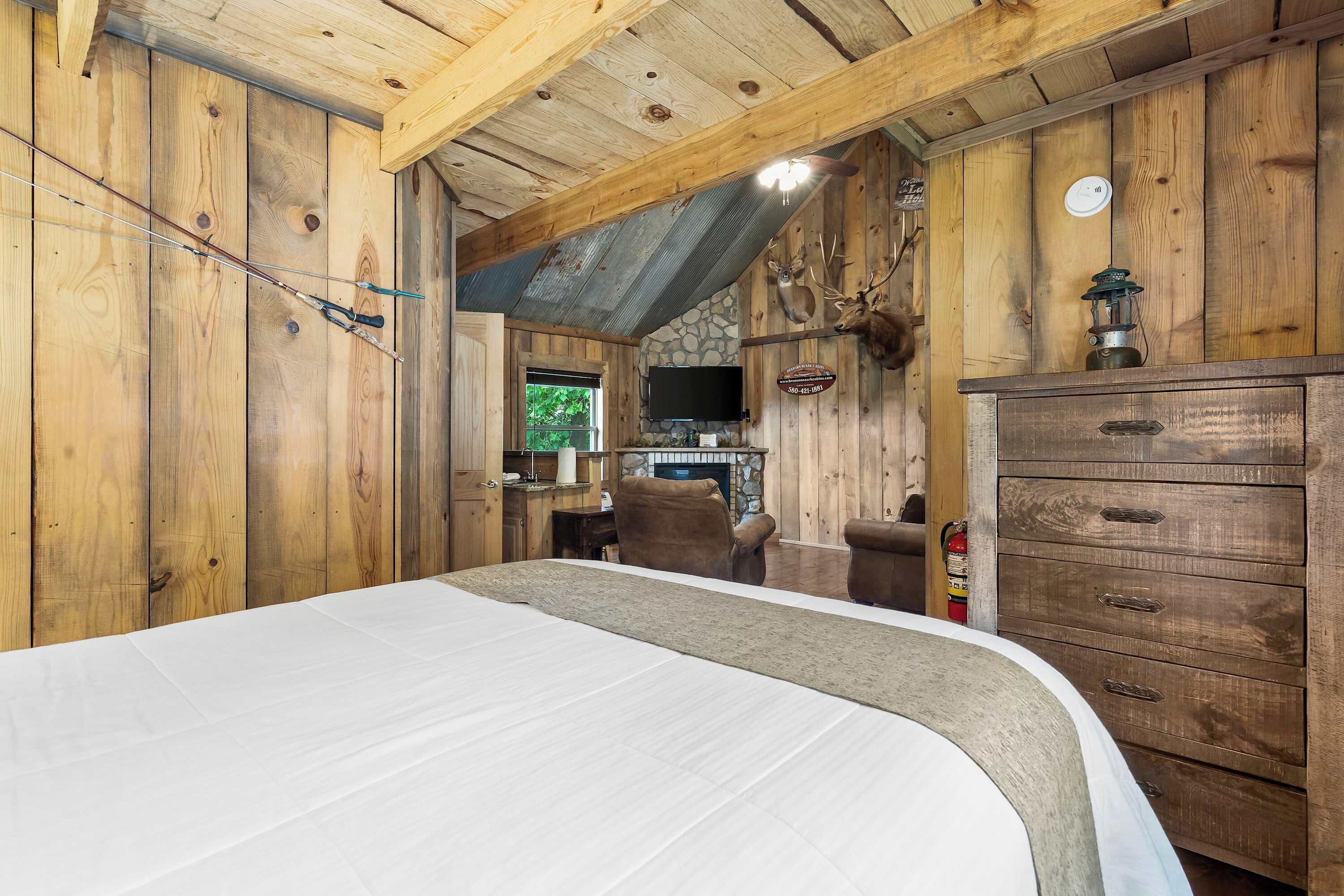 Interior de una cabaña de madera con una cama, una chimenea, un televisor y una cornamenta de ciervo en la pared.