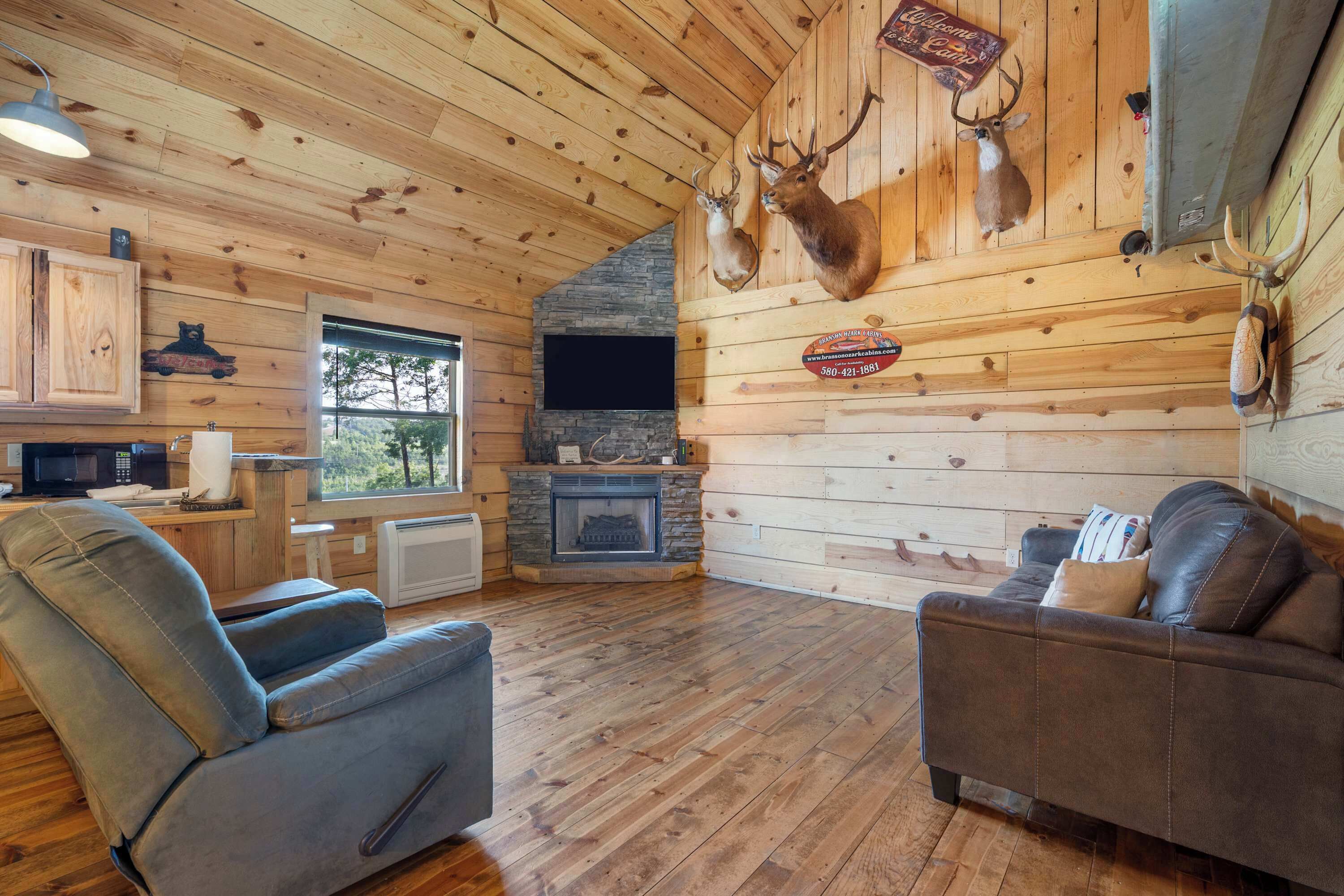 A log cabin interior with a fireplace, wooden walls, and mounted deer heads.