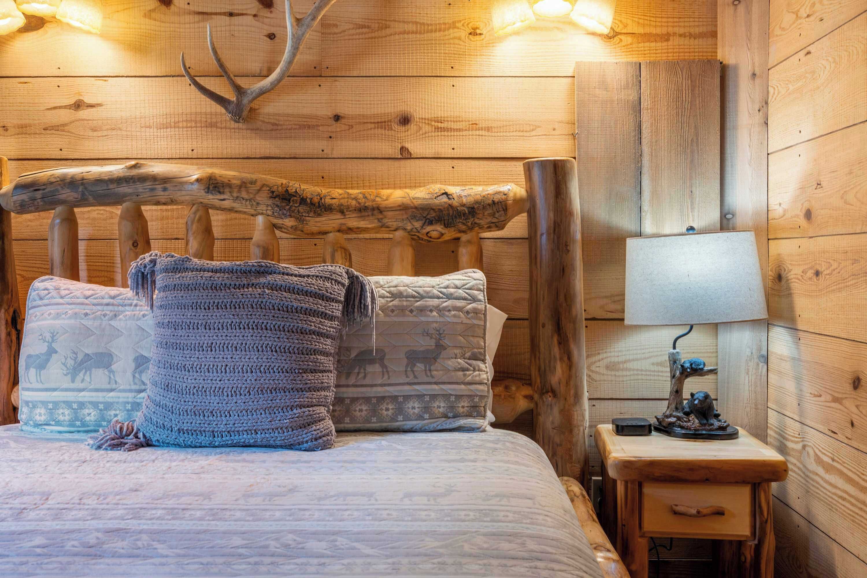 A wooden bed with a carved headboard, two patterned pillows, a bedside lamp, and a small wooden nightstand.