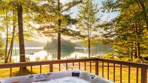 A hot tub on a deck overlooking a lake with trees and boats. - Hot Tub, Water Amenities, Lakeshore Cottage (Newaygo)