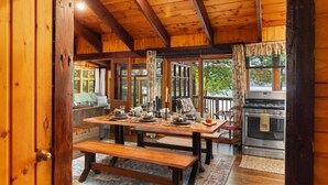 A wooden cabin interior with a dining table set for four, a bench, and a kitchen area with a stove. - Hot Tub, Water Amenities, Lakeshore Cottage (Newaygo)
