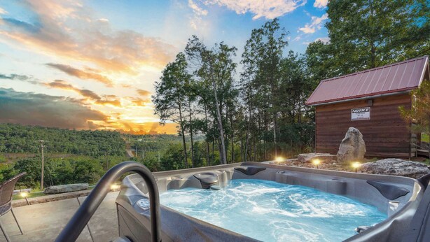 A hot tub with a view of a sunset and a wooden cabin in the background. - Antlers Lodge - Cabin for 4 (Branson)