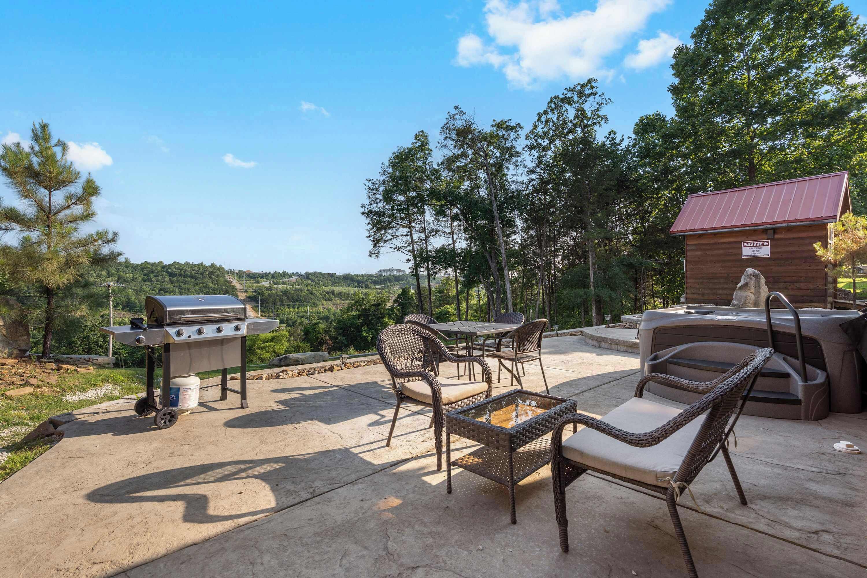 Une terrasse extérieure avec un barbecue, des chaises en osier, un jacuzzi et, au fond, un chalet en bois.
