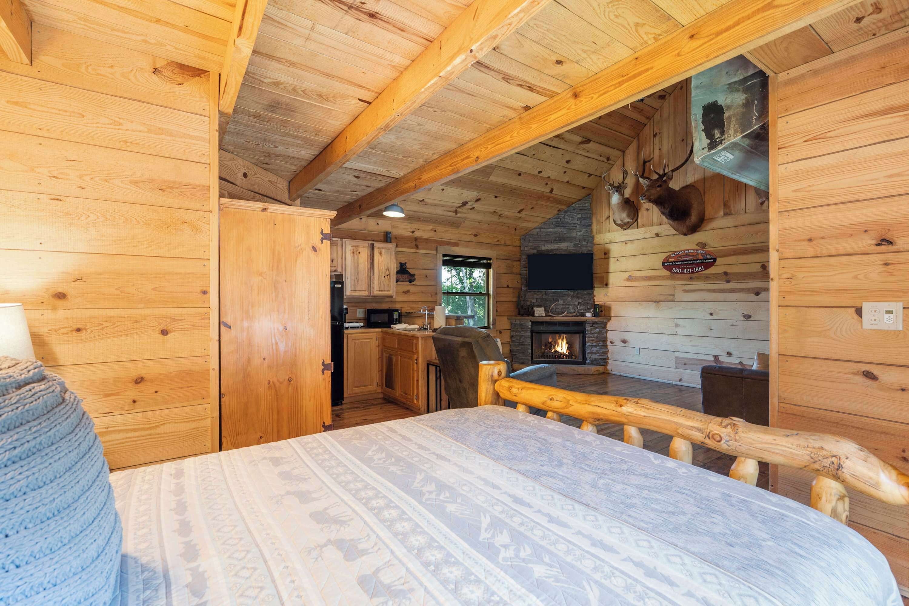 Ein Blockhaus-Interieur mit einem Bett, Holzwänden, einem Kamin aus Stein und einem aufgehängten Hirschgeweih.