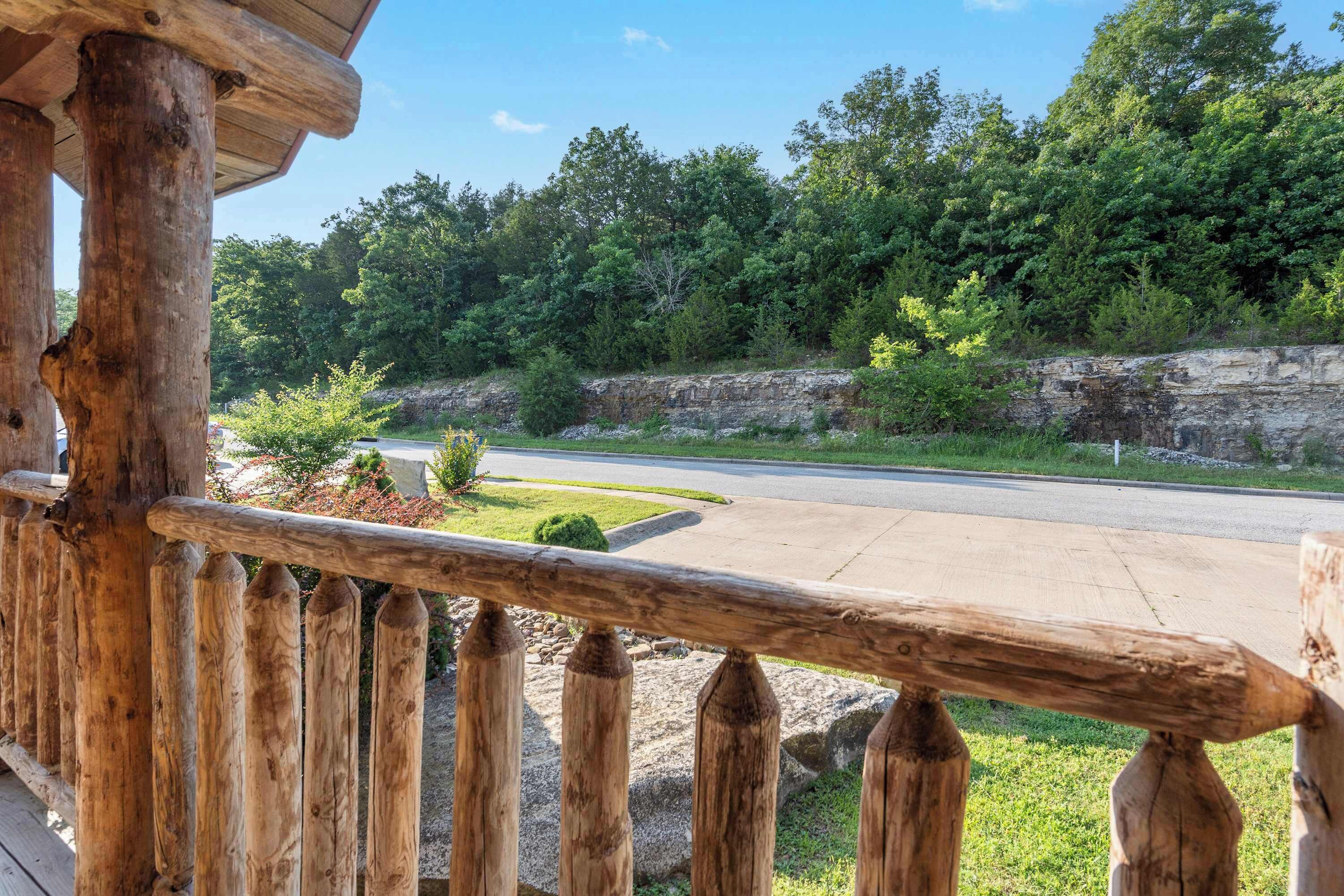 A wooden deck with a view of a road and a forested area.