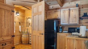 A wooden cabin interior with a black refrigerator, wooden cabinets, a wooden bar stool, and a wooden ceiling. - Antlers Lodge - Cabin for 4 (Branson)