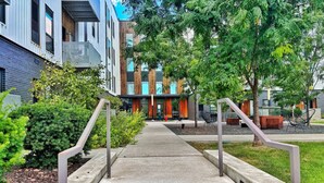 A concrete staircase leading to a building with a modern design, surrounded by greenery and outdoor seating areas. - Your home away from home (Des Moines)