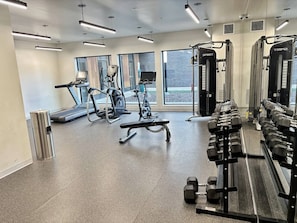 A modern gym with treadmills, elliptical machines, a bench press, and a rack of dumbbells. - Your home away from home (Des Moines)