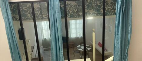 A room with a sliding glass door featuring blue curtains, a patterned wallpaper, and a view of a dining area with a table and chairs.