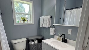 A bathroom with a toilet, sink, and mirror. There is a window above the toilet and a towel rack above the sink.
