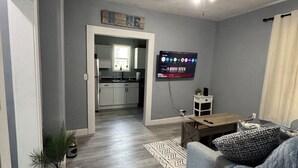 A modern living room with a grey sofa, a ceiling fan, and a flat-screen TV mounted on the wall.