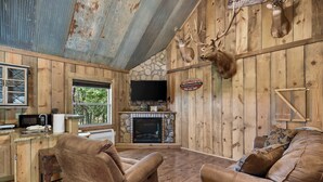 L’intérieur d’un chalet rustique, avec une cheminée en pierre, des murs en bois, des têtes de cerf accrochées aux murs, un téléviseur et des fauteuils inclinables en cuir.