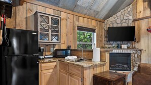 Une cuisine compacte avec des meubles en bois, un réfrigérateur noir, un four à micro-ondes et une cheminée en pierre.