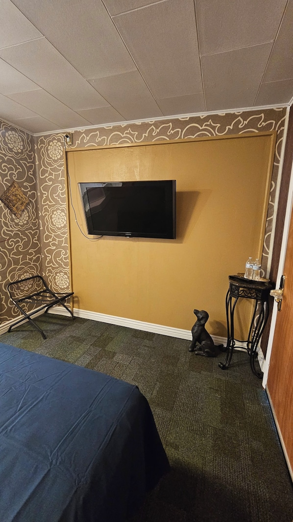 Una habitación con una cama, un televisor montado en la pared, una mesita con botellas de agua y un diseño decorativo en la pared.
