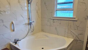 Une salle de bain moderne avec une baignoire sur pieds, une douchette et une fenêtre équipée de stores.
