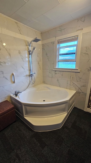 Un baño moderno con una bañera independiente, un cabezal de ducha manual y una ventana con persianas.