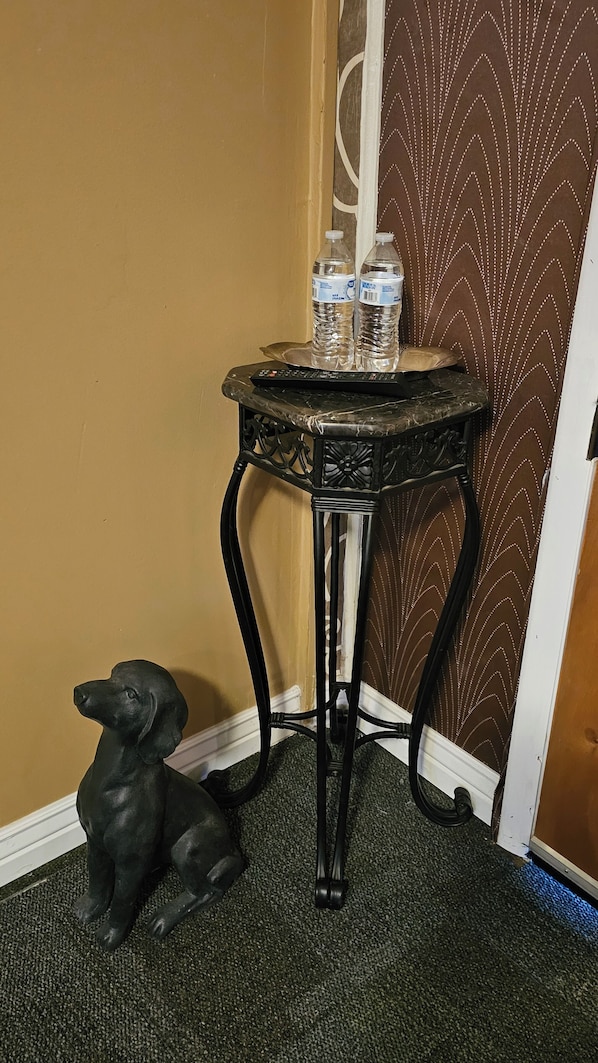 A corner with a black metal table holding two water bottles and a remote control, a black dog statue, and a patterned wall. - Charming motel in Powder River WY
Located minutes from Hells Half Acre must see (Casper)