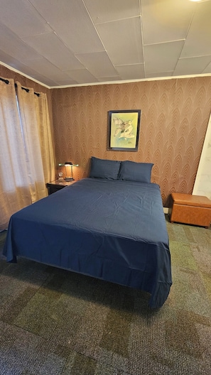A hotel room with a large bed, a nightstand with a lamp, a small table, and a framed picture on the wall. - Charming motel in Powder River WY
Located minutes from Hells Half Acre must see (Casper)
